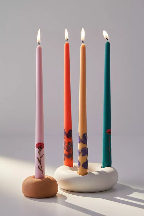 A vibrant collection of lit candles in shades of pink, orange, yellow, and teal, casting a warm and inviting light.