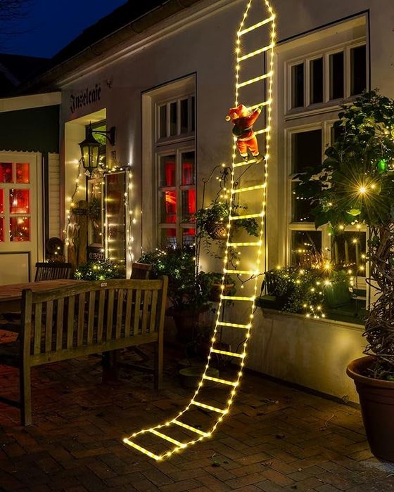 The ladder adorned with warm white lights hanging from the side of a house