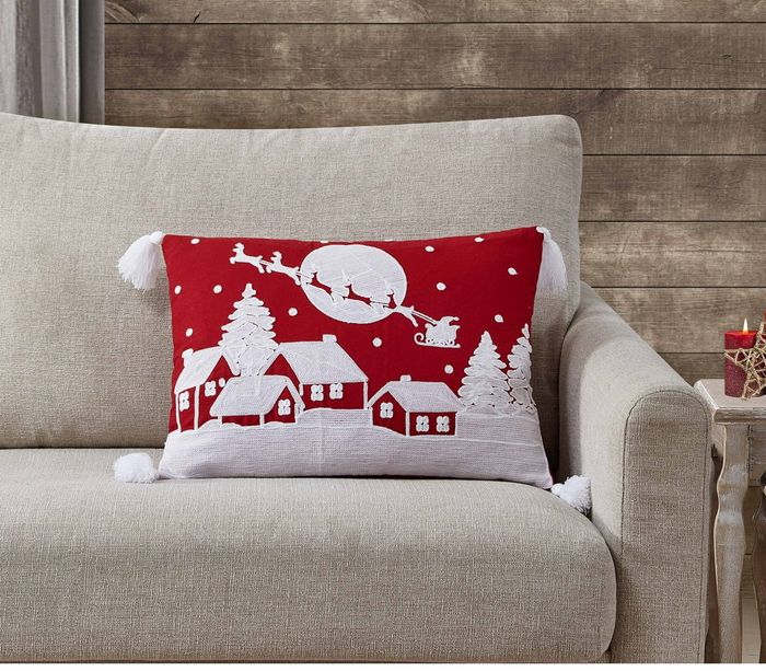 A red throw pillow with white houses and Santa's sleigh design.