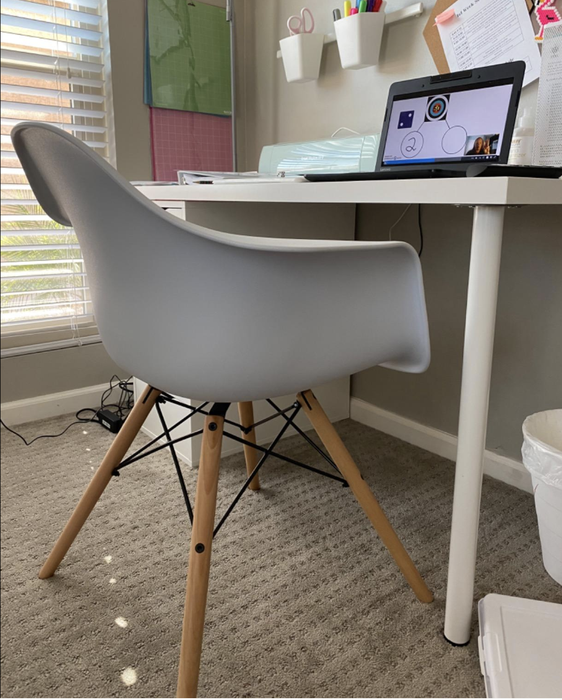 A white office chair with four light brown legs positioned in front of a desk.