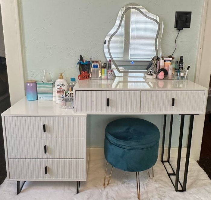Vanity desk showcasing makeup, skincare products, and a distinctive mirror. Includes a teal stool and a well-organized beauty area, perfect for inspiring home decor ideas