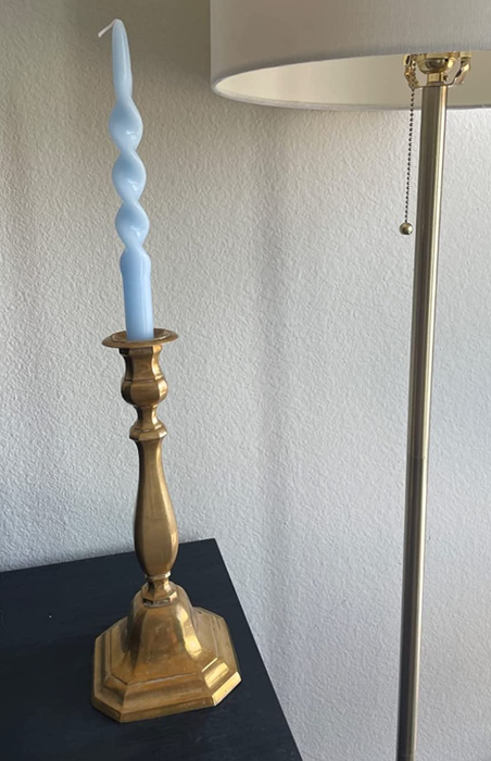 A reviewer’s image of a blue spiral candle placed in a gold candelabra on a black table beside a floor lamp