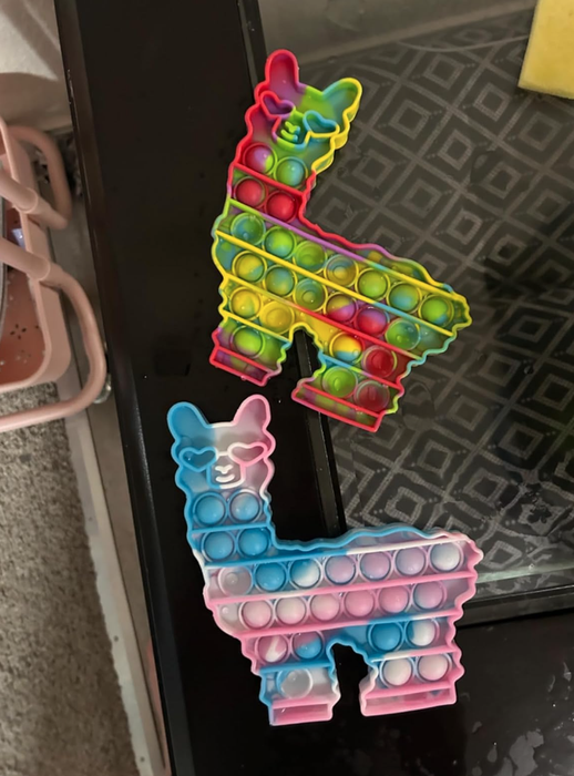 Two llama-shaped pop-it toys sit on a table, one with vibrant multicolored sections and the other with soft pastel hues.