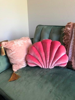 a pink shell pillow resting on a green velvet couch