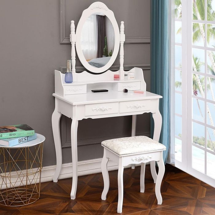White vanity set with a mirror and cushioned stool, showcasing makeup items and a book on a nearby table, positioned near a window with a picturesque view