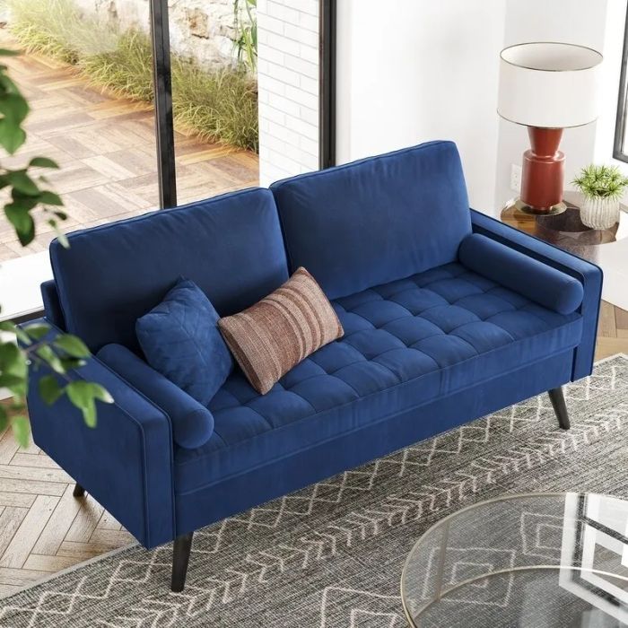 A modern blue sofa with tufted cushions and two decorative pillows sits gracefully in a bright, sun-filled room near a large window