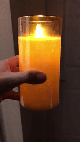 A glowing candle encased in a gold-hued, translucent glass holder, held in the reviewer's hand.