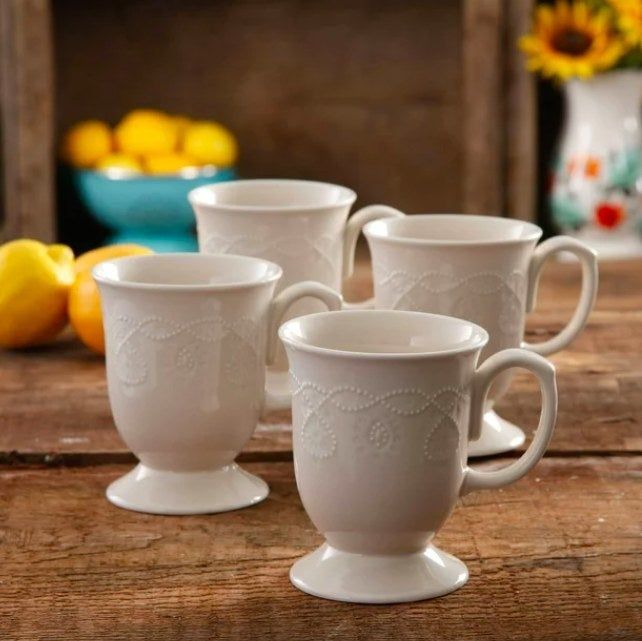 A set of four white mugs displayed on a wooden table, adding a touch of elegance.