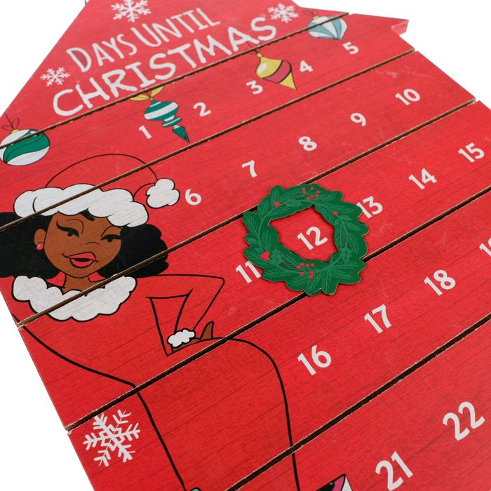 A house-shaped Advent calendar adorned with a movable wreath and an illustrated woman dressed in a festive, Santa-themed outfit.