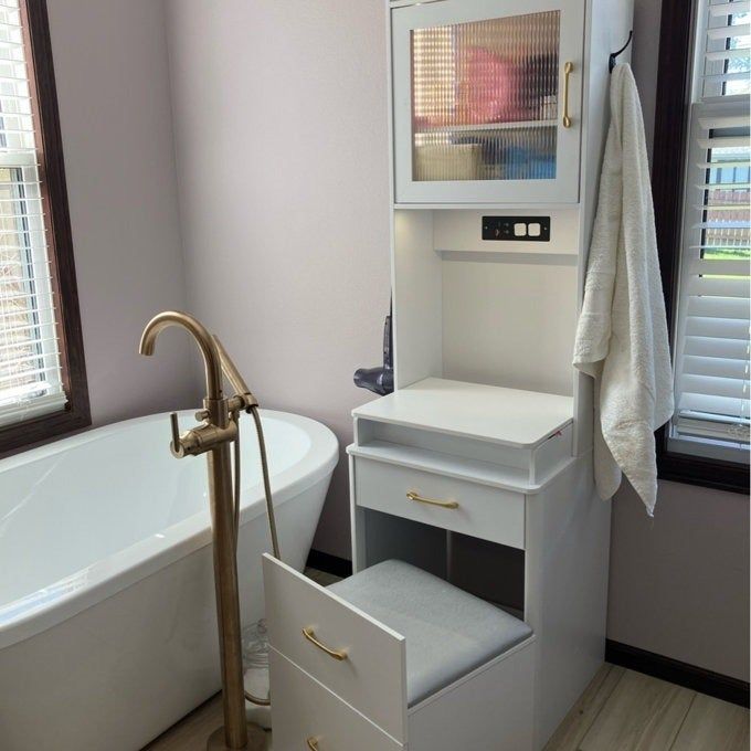 Bathroom featuring a freestanding bathtub and a sleek vanity complete with a stool, towel rack, and storage drawers adorned with brass handles
