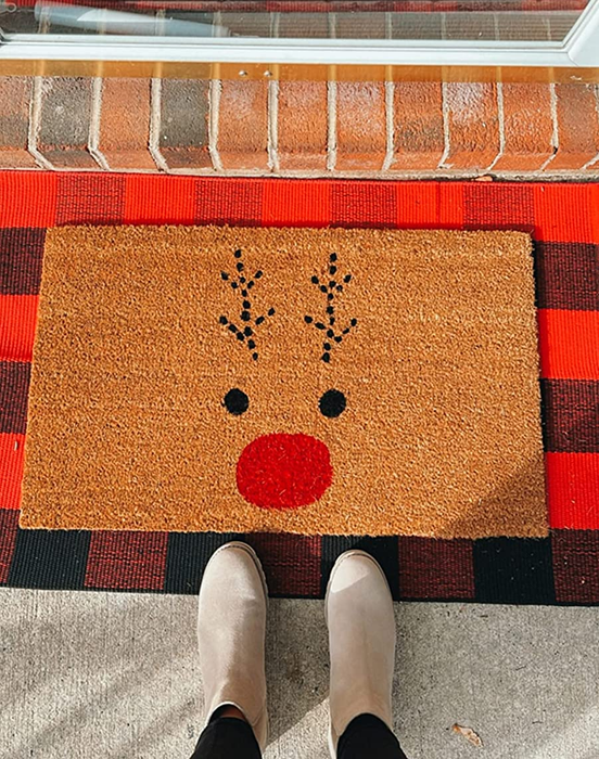 reviewer standing in front of the Rudolph doormat, which sits on top of a red and black buffalo plaid mat