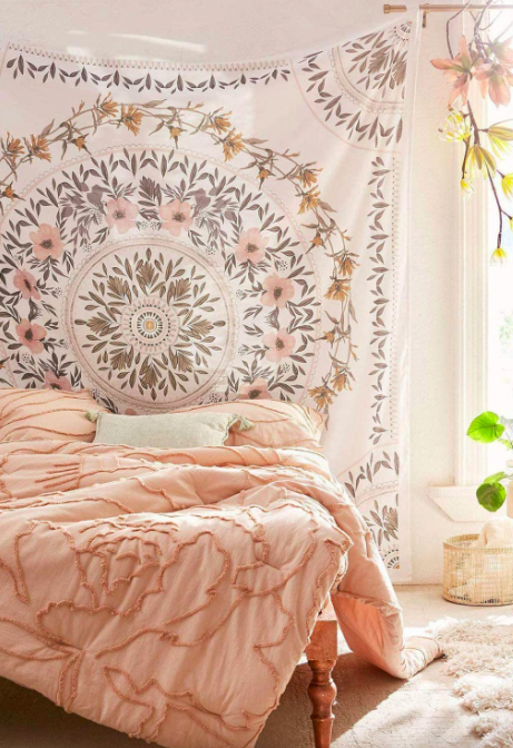 A pink and white floral medallion tapestry draped over the wall above a bed with a matching pink comforter.