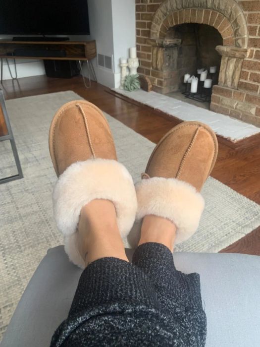 A customer review photo showing someone relaxing with their feet up, comfortably wearing the shearling-lined slippers.