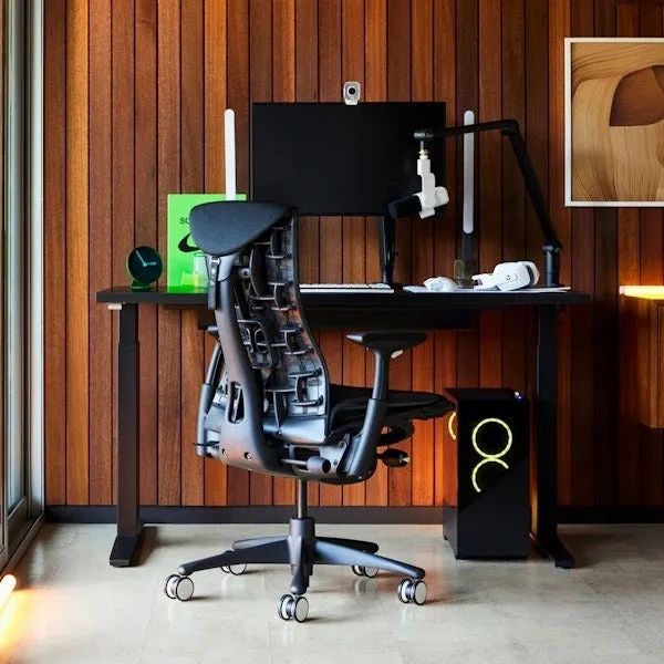 A sleek office setup featuring a stylish ergonomic chair, a height-adjustable desk, a computer monitor, and a modern wooden backdrop