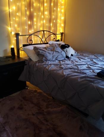 The lights are draped over a curtain, positioned behind a bed, casting a soft glow.