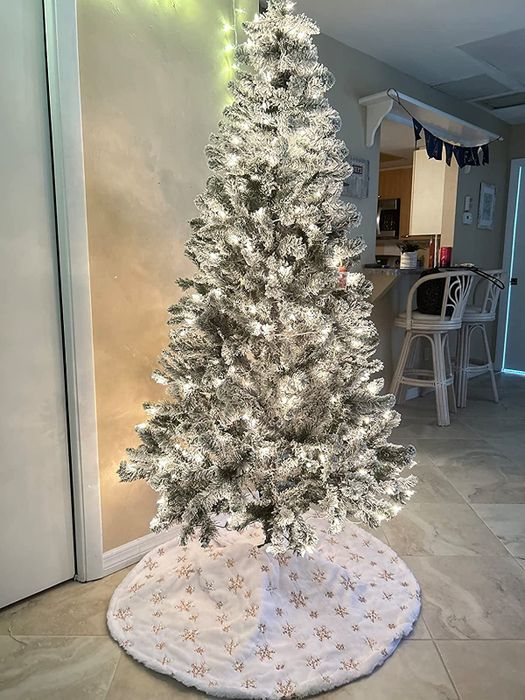 A reviewer's flocked tree with a white faux fur tree skirt underneath, decorated with gold snowflakes.