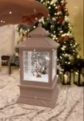 A gif of a reviewer holding up the glowing, snowing lantern in front of a decorated Christmas tree
