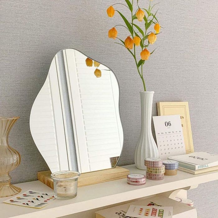 A petite, cloud-shaped standing mirror resting on a wooden base.