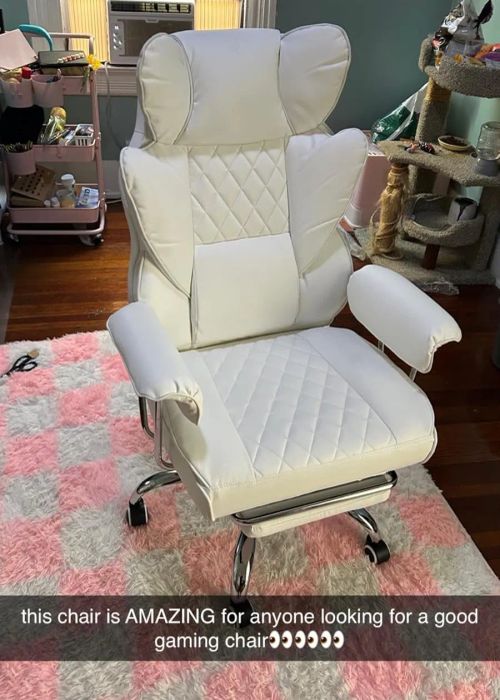 A stylish white gaming chair placed in a room with a window, a desk, and a cat tree. The text highlights the chair's comfort and its suitability for gaming.