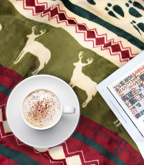 overhead shot of a mug and magazine resting on the reindeer throw blanket, showing off its print up close