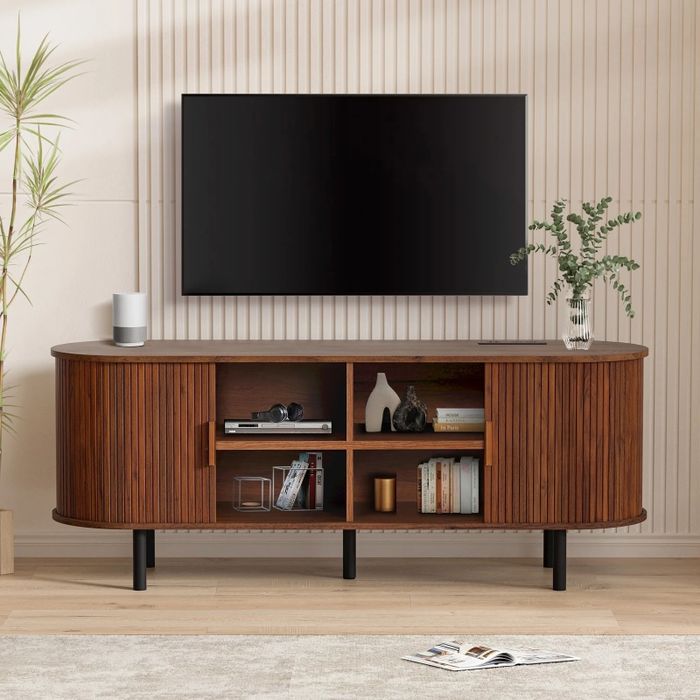 A modern living room featuring a sleek wooden TV stand, a large flat-screen TV mounted on the wall, decorative items arranged on shelves, and a plant placed nearby.
