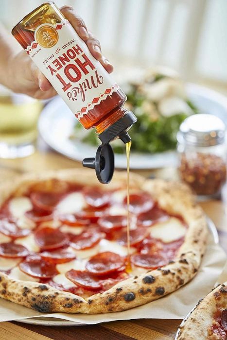 Someone drizzling Mike's Hot Honey over a pizza