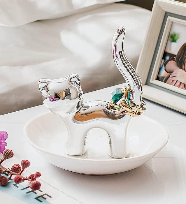 A silver cat-shaped trinket dish with a ring balanced on its tail.