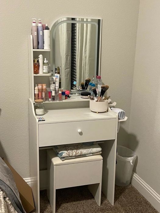 Vanity table equipped with a mirror, shelves stocked with beauty products, brushes, and a small stool, perfect for organizing makeup and skincare items