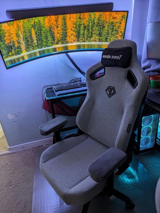 Gaming chair setup with a large curved monitor displaying a beautiful forest scene, with the keyboard neatly placed below the screen on the desk