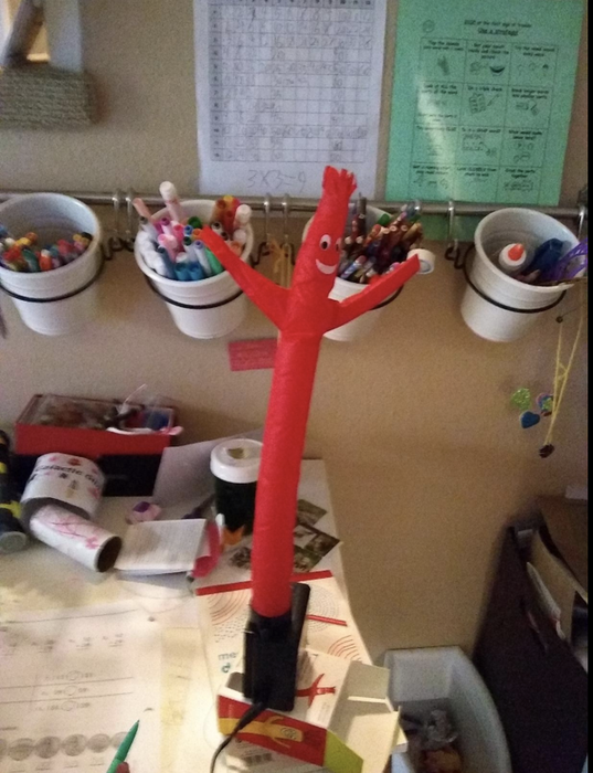 A red inflatable figure perched on a desk