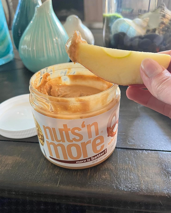 A reviewer dipping a crisp apple into the jar of white chocolate pretzel peanut butter.