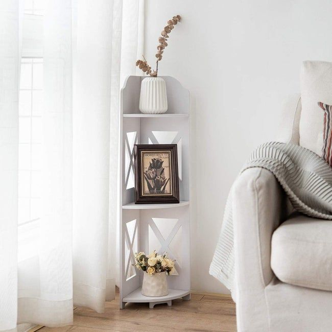 A compact white corner shelf unit with three levels, holding potted plants and framed pictures