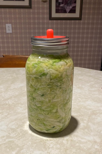 A jar of homemade sauerkraut with a special fermentation lid, placed on a kitchen table, ideal for fermentation enthusiasts or DIY aficionados.