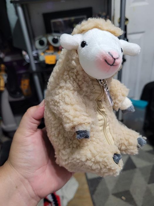 A person holding a plush sheep with a zipper, possibly a coin purse or small bag.