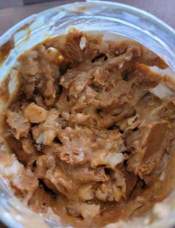 The open jar of peanut butter revealing candy pieces nestled inside.