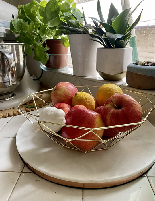 A gold geometric wire bowl sitting on a counter, filled with fresh fruit for a chic and modern touch.