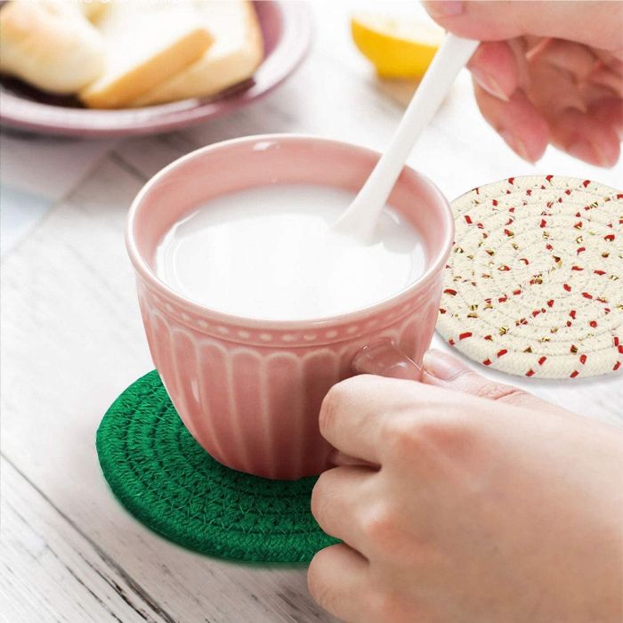 hands placing a mug on one of the green coasters, with a red-and-white coaster beside it