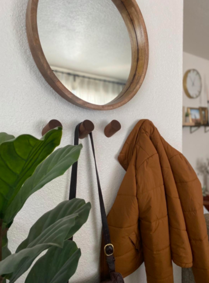 Dark brown wall hooks supporting a black purse and a red coat, placed beneath a mirror.