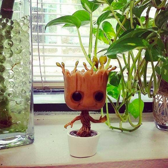 A cute tree-inspired figurine sitting in a pot, placed on a windowsill among live plants, making it a charming addition to any home decor.