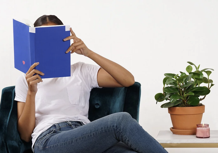 model reading a book with a blue cover beside a potted plant
