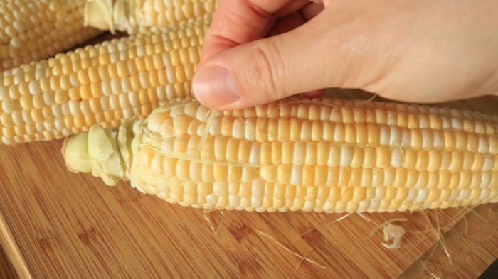 Manually peeling the silk from an ear of corn.