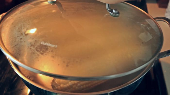 A hand places a lid on a pot containing corn.