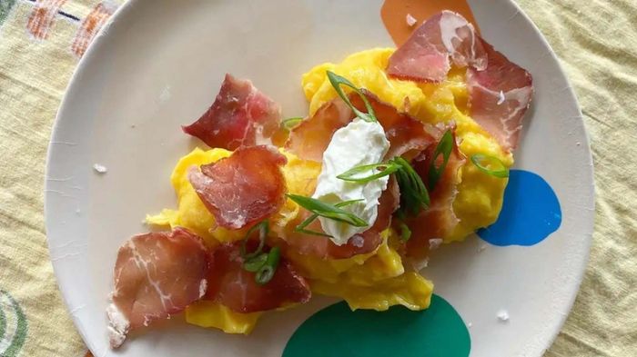 A plate of scrambled eggs garnished with thinly sliced meat, a dollop of sour cream, and a sprinkle of chives
