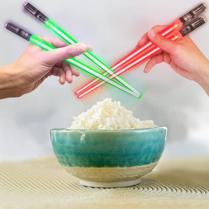 Two hands using the red and green lightsaber chopsticks to scoop up rice.