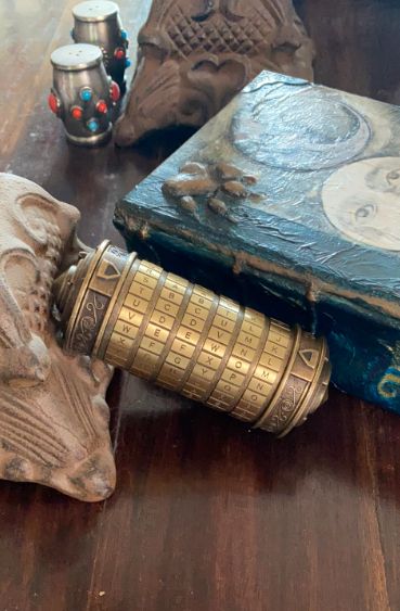 An intricately designed brass cipher device sits elegantly on a table, surrounded by antique artifacts and a weathered old book.
