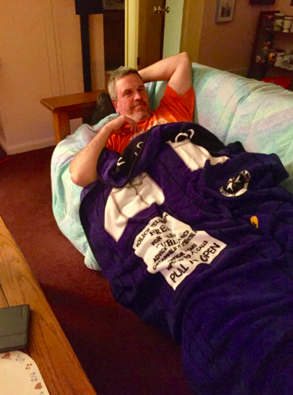 A person lounging on a couch, wrapped in a cozy TARDIS-themed blanket, combining comfort with fandom-inspired home decor.
