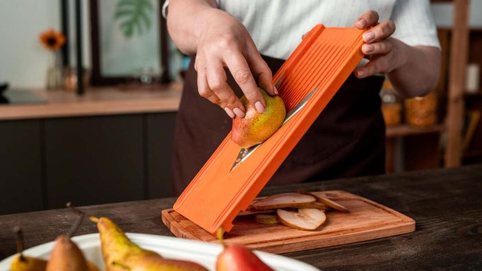 A chef is pictured skillfully slicing a pear into thin pieces using a mandoline slicer