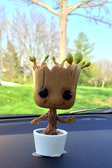 A bobblehead of a tree-like character dancing in a small pot, placed on a car dashboard, bringing fun and whimsy to the ride.