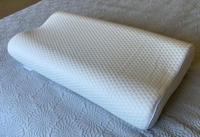 A contoured memory foam pillow with a textured surface placed on a neatly made bed, designed to provide ergonomic support for a night of comfortable sleep.