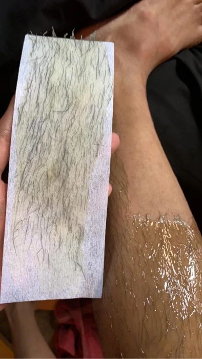 Reviewer holds a used wax strip with a bare patch on their leg.